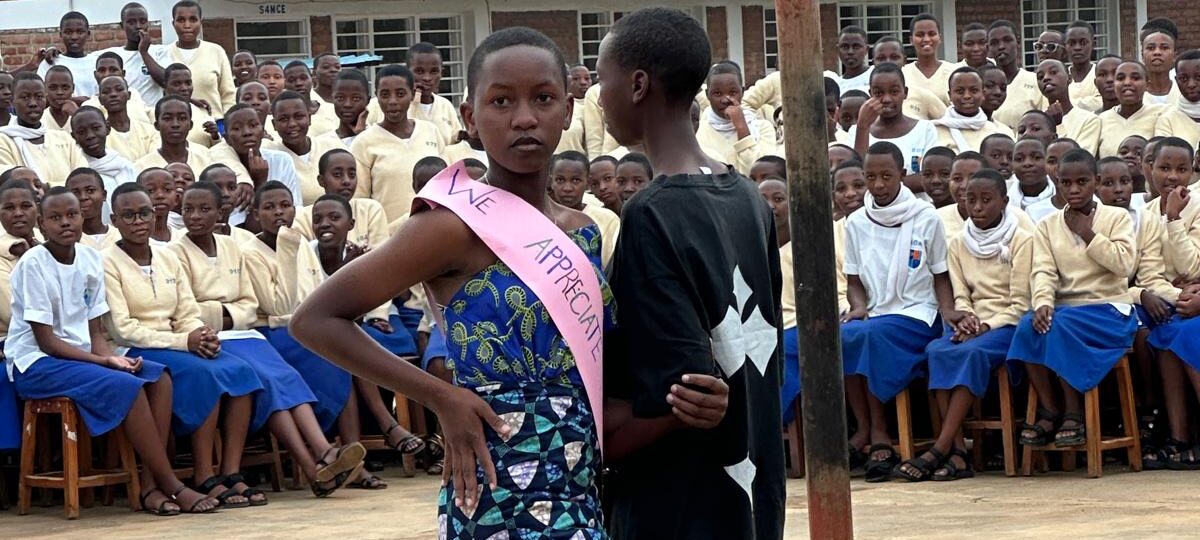 Das Foto zeigt ein tanzendes Paar in Ruanda. Im Hintergrund sind zahlreiche Schülerinnen zu erkennen. Sie schauen dem Tanzpaar zu.